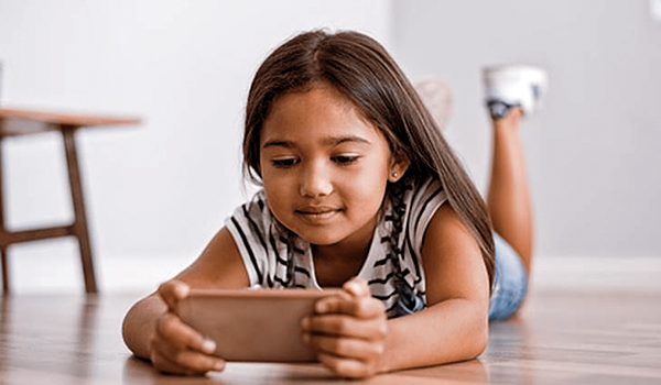Little asian girl lying on floor using mobile phone to play. Multiethnic female child watching cartoon on smartphone at home. Childhood and moder technology concept.